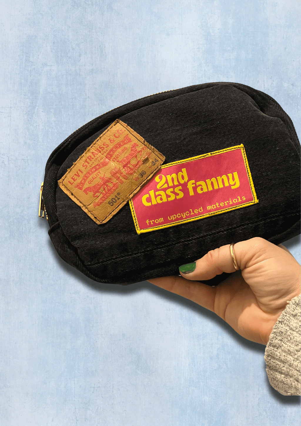 Black pouch with '2nd class fanny' label held by a hand on a light blue background
