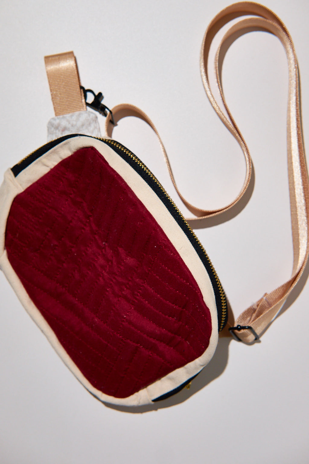 Small bag with a red front panel and beige strap upcycled from comforter on a light gray background