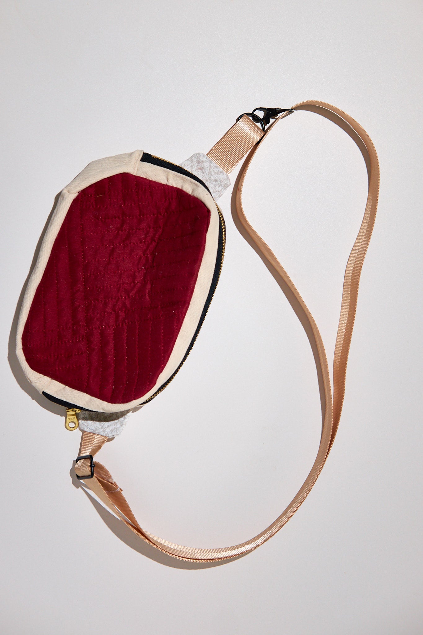 Small bag with a red exterior and beige strap upcycled from comforter on a light gray background