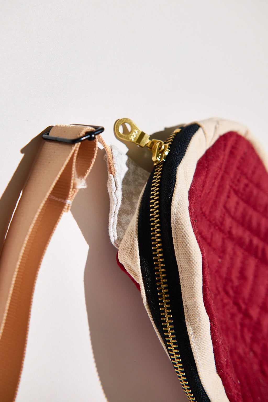 Close-up of a textured red pouch with a zipper and strap upcycled from a comforter on a light background