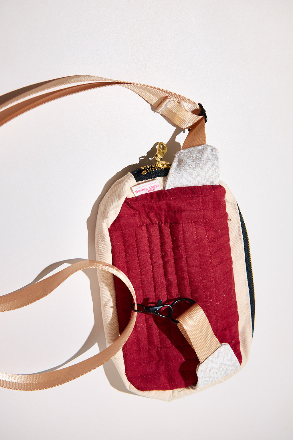 Crossbody bag with a red exterior and beige strap upcycled from a comforter on a white background