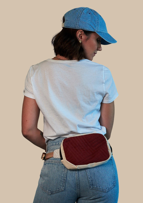 Person wearing a blue cap and light blue shirt with a red and beige fanny pack upcycled from comforter on a beige background