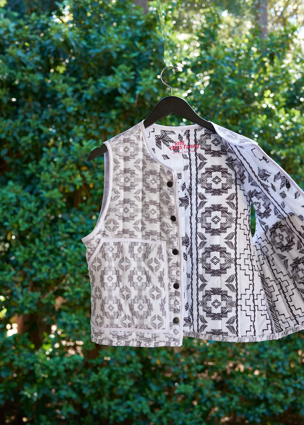 Patterned vest from upcycled comforter on a hanger against a green leafy background