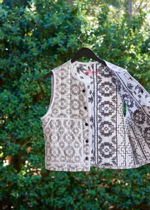 Patterned vest from upcycled comforter on a hanger against a green leafy background