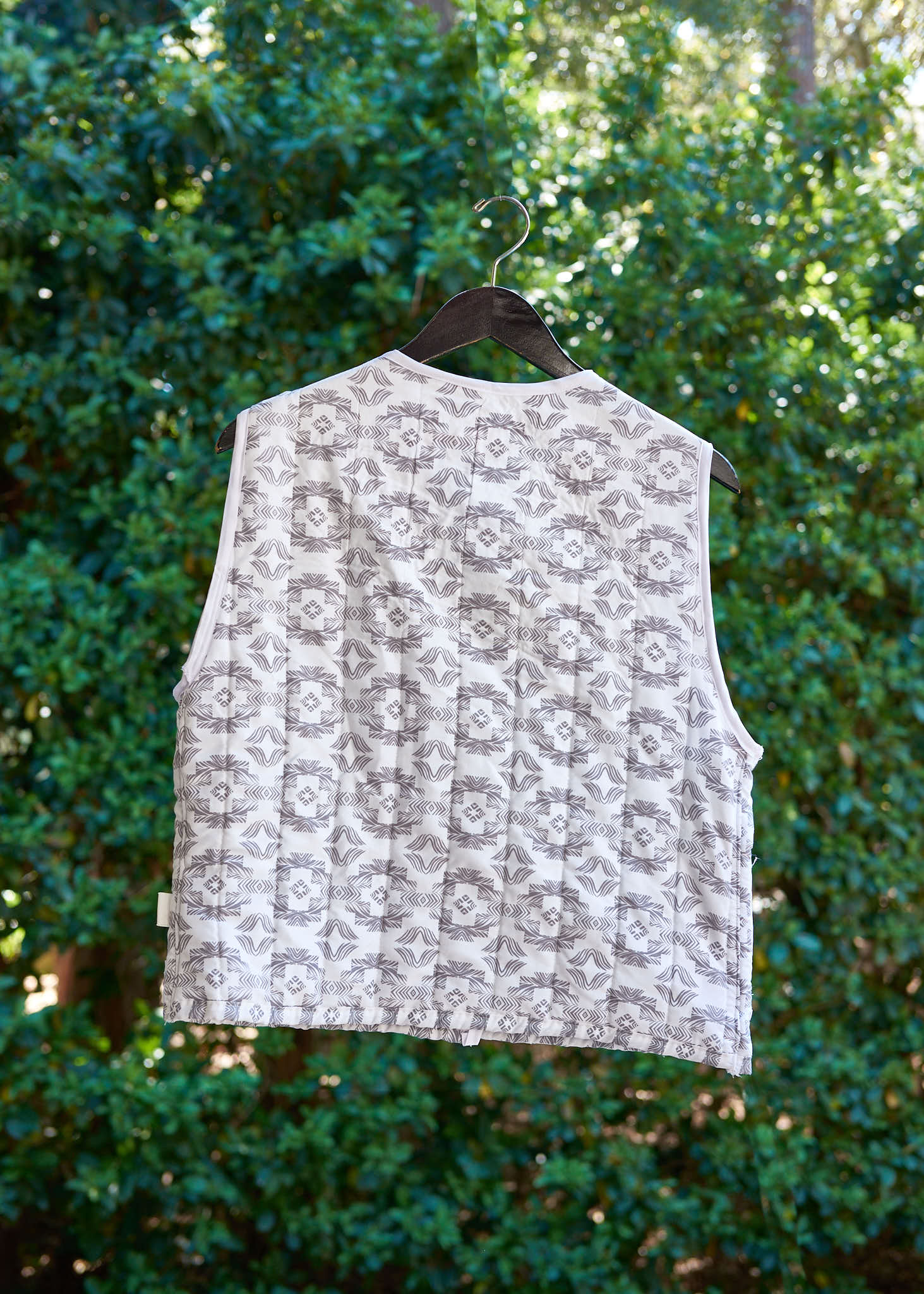 Patterned vest from upcycled comforter on a hanger against a green bush background