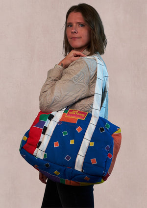 Person holding a geometric pattern duffle bag on the shoulder upcycled from comforter on a beige background