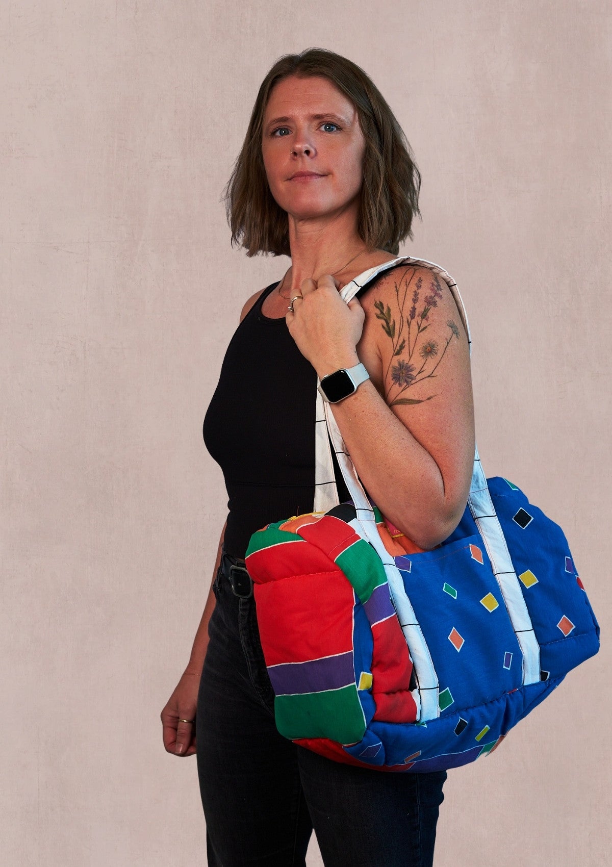 Person holding a colorful quilted bag upcycled from comforter against a beige background