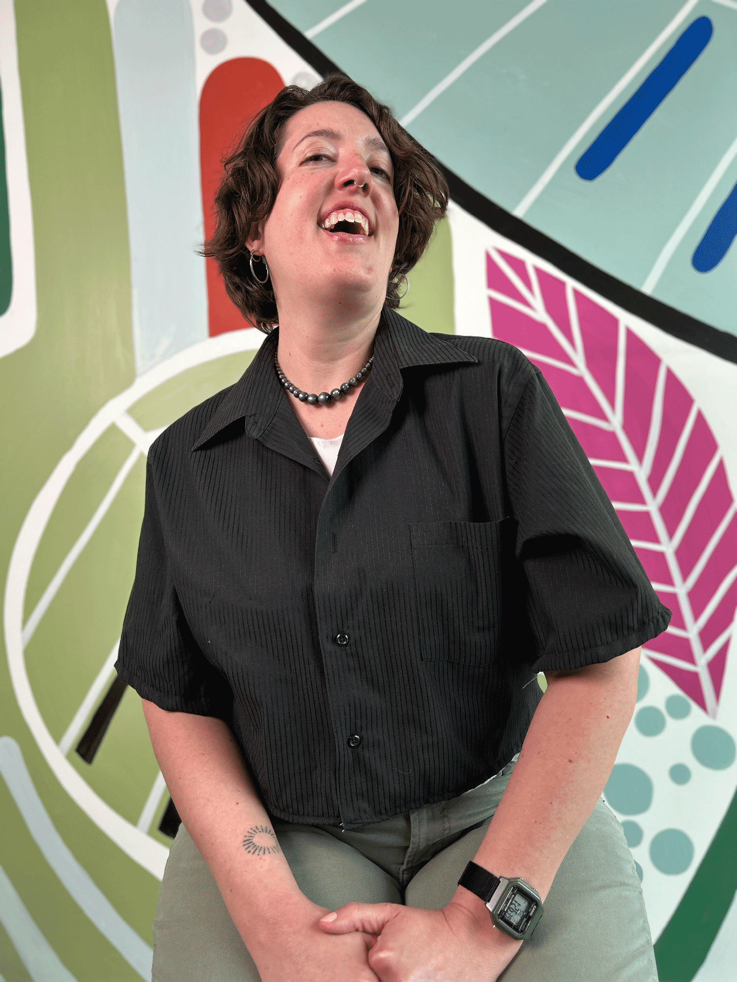 Person wearing a black shirt upcycled from a dress shirt sitting in front of a colorful abstract background