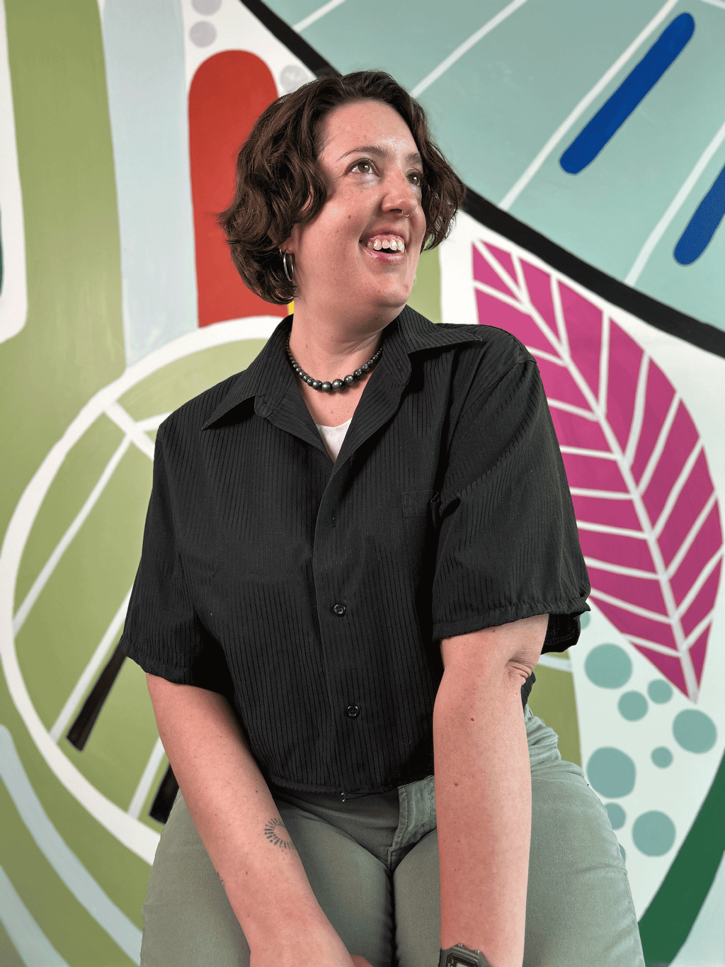 Person wearing a black shirt upcycled from a dress shirt in front of a colorful abstract mural