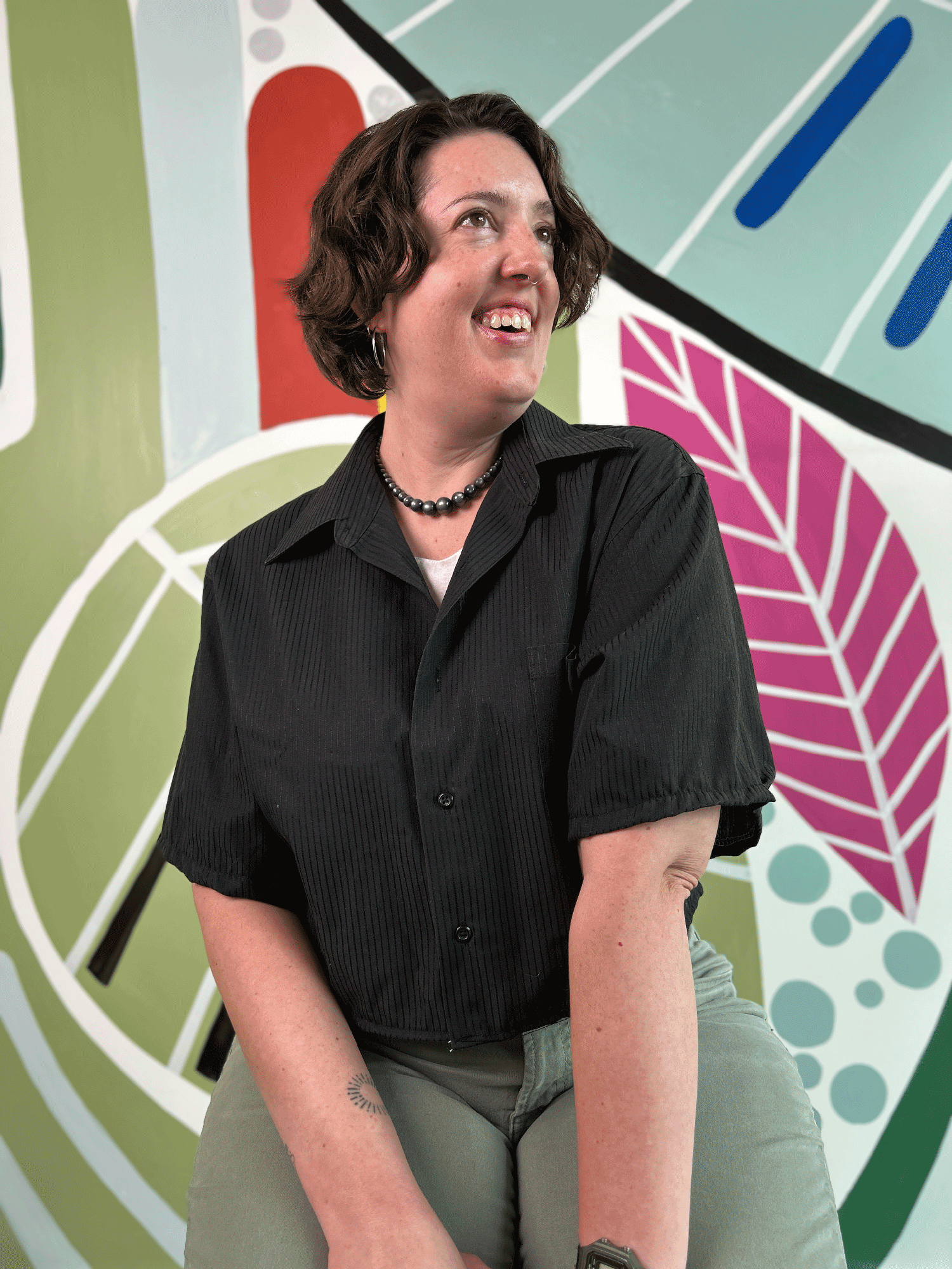 Person wearing a black shirt upcycled from a dress shirt in front of a colorful abstract mural