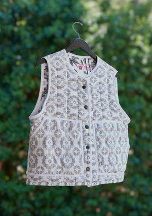 White patterned vest from upcycled comforter on a hanger against a green leafy background