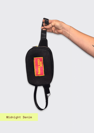 Black waist bag with a colorful label reads 2nd Class Fanny held by a hand on a light gray background