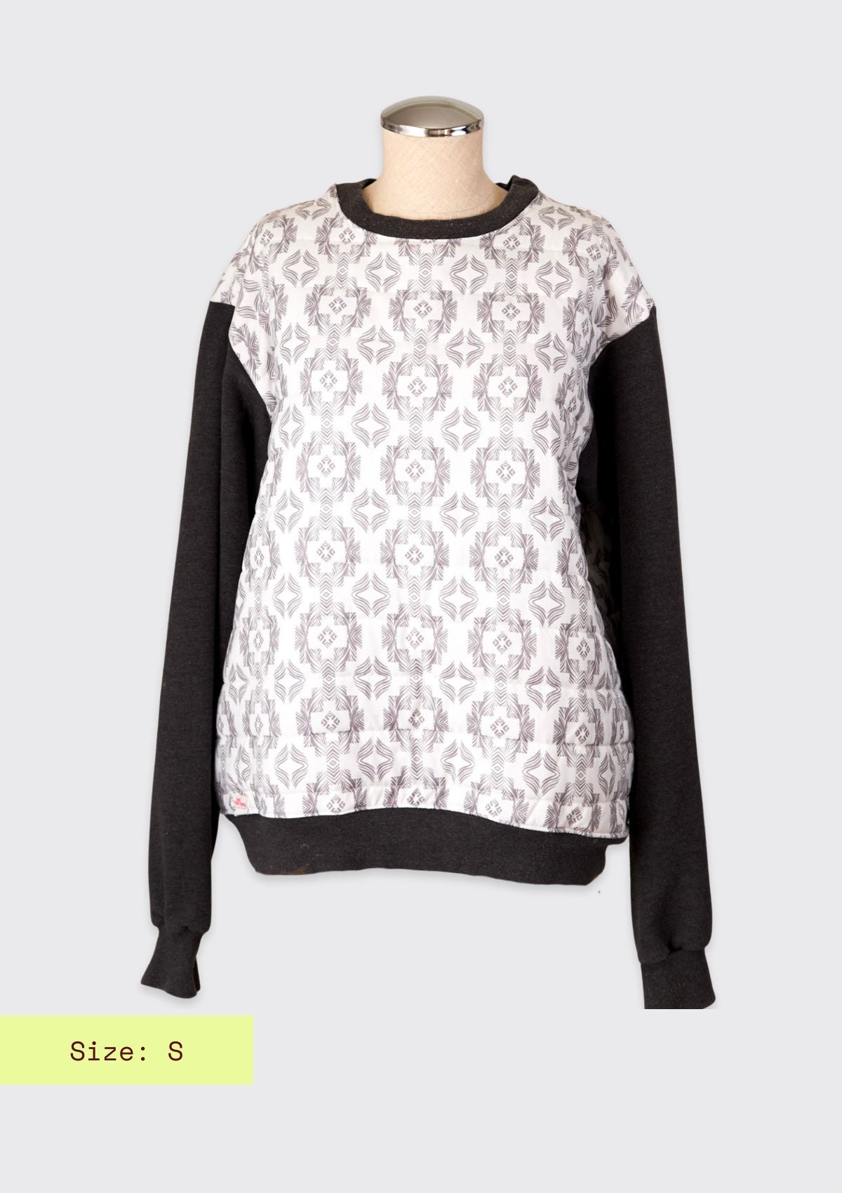 Sweater with black sleeves and white pattern on a mannequin upcycled from comforter against a light gray background