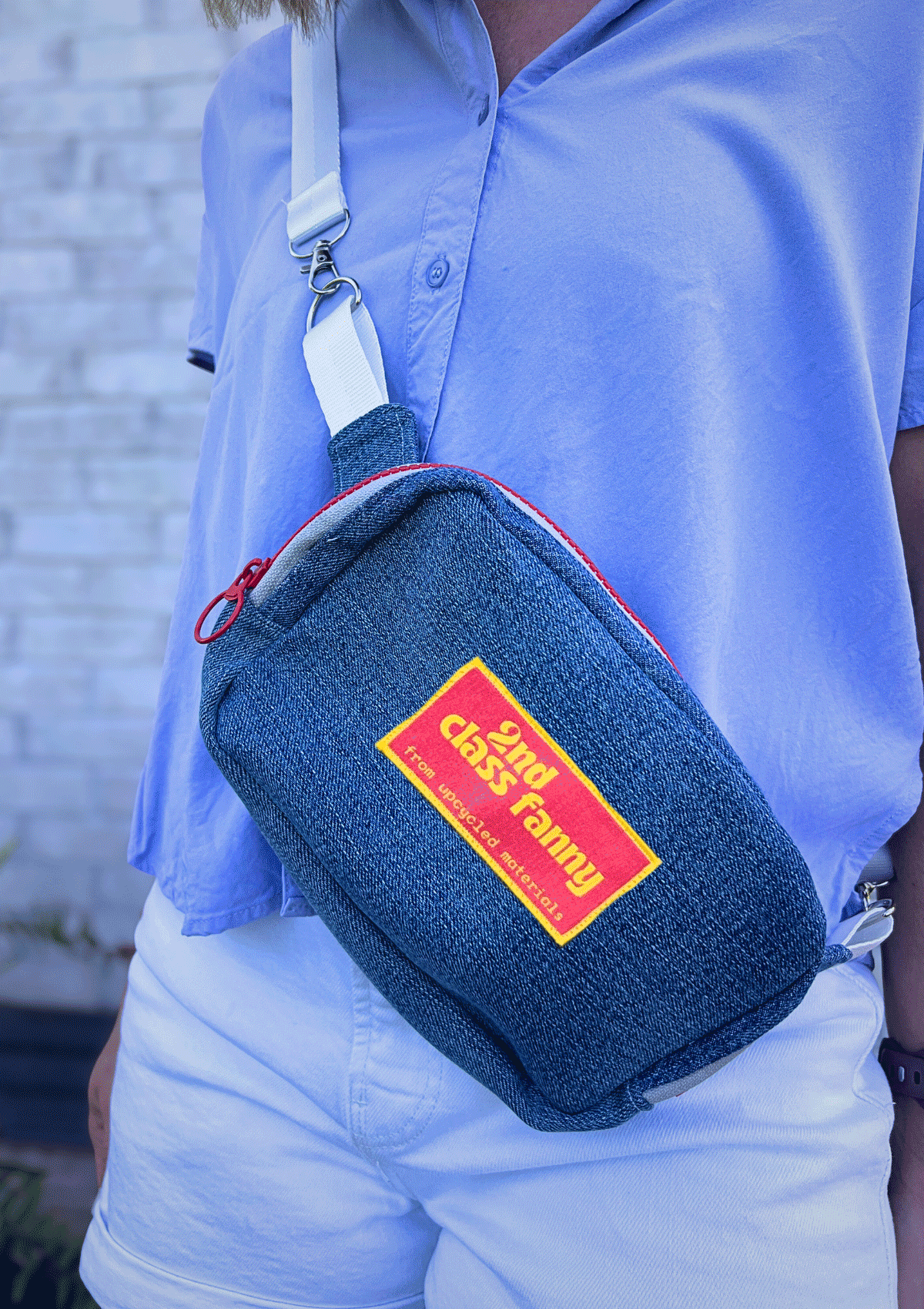 Person wearing a blue crossbody bag with a visible brand logo against a light blue shirt.
