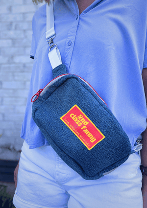 Person wearing a blue crossbody bag with a visible brand logo against a light blue shirt.
