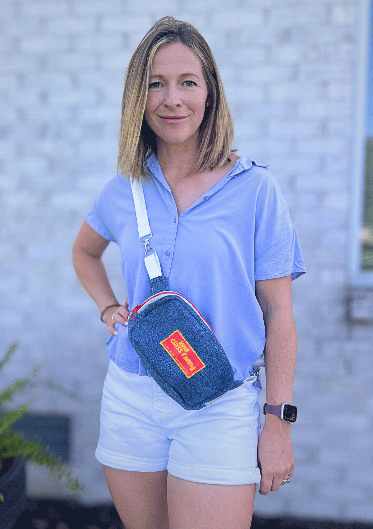 Woman wearing a blue shirt and white shorts with a blue denim crossbody bag outdoors.