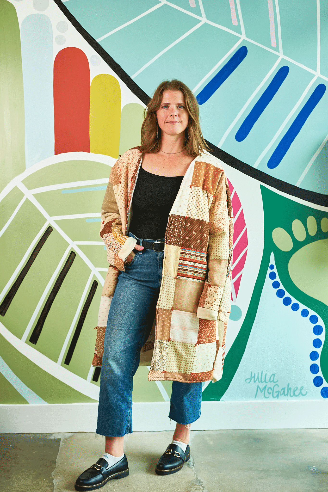 Woman standing in front of a colorful mural wearing a patterned cardigan.