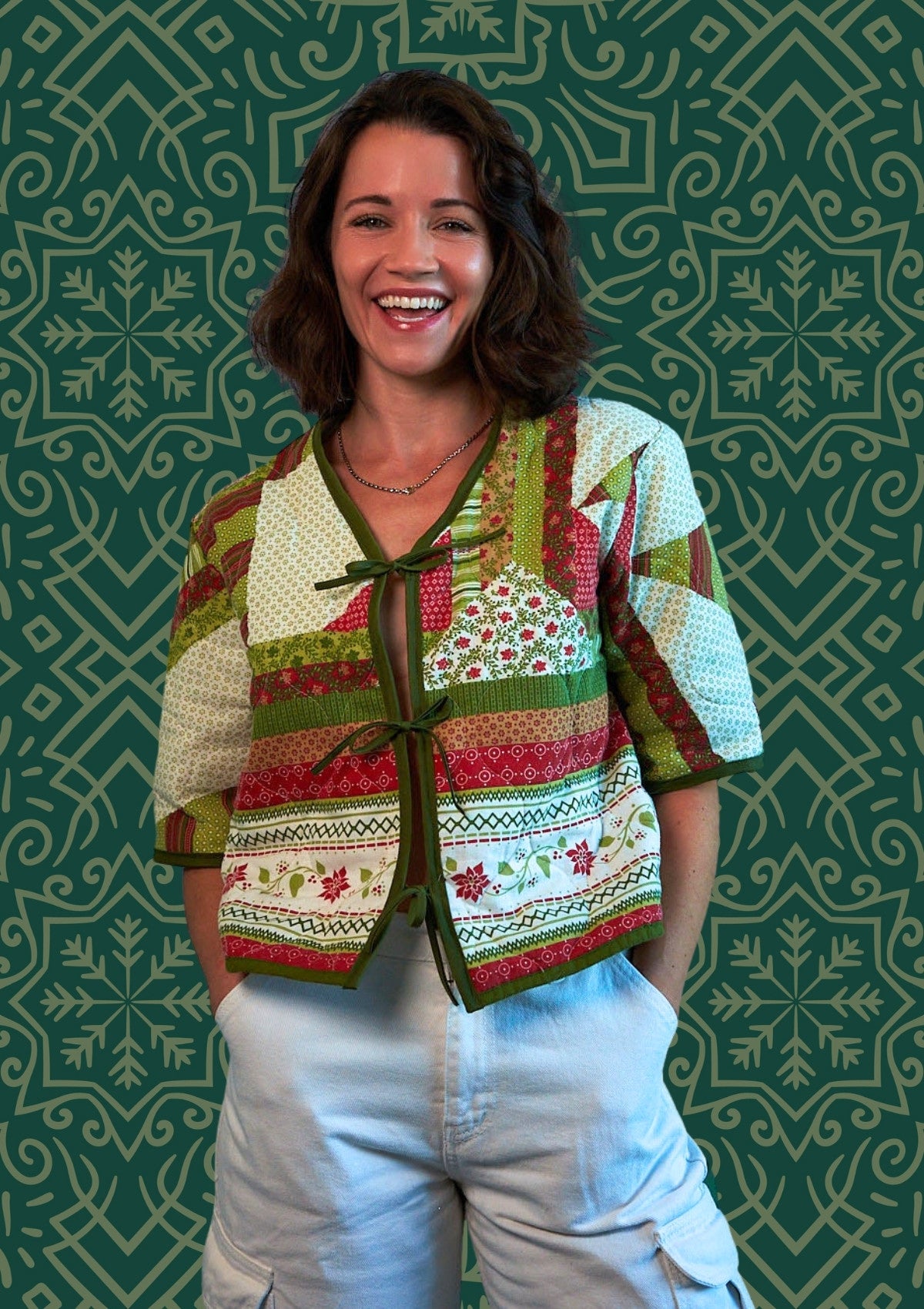 Woman wearing a colorful patterned holiday jacket upcycled from comforter against a green patterned background