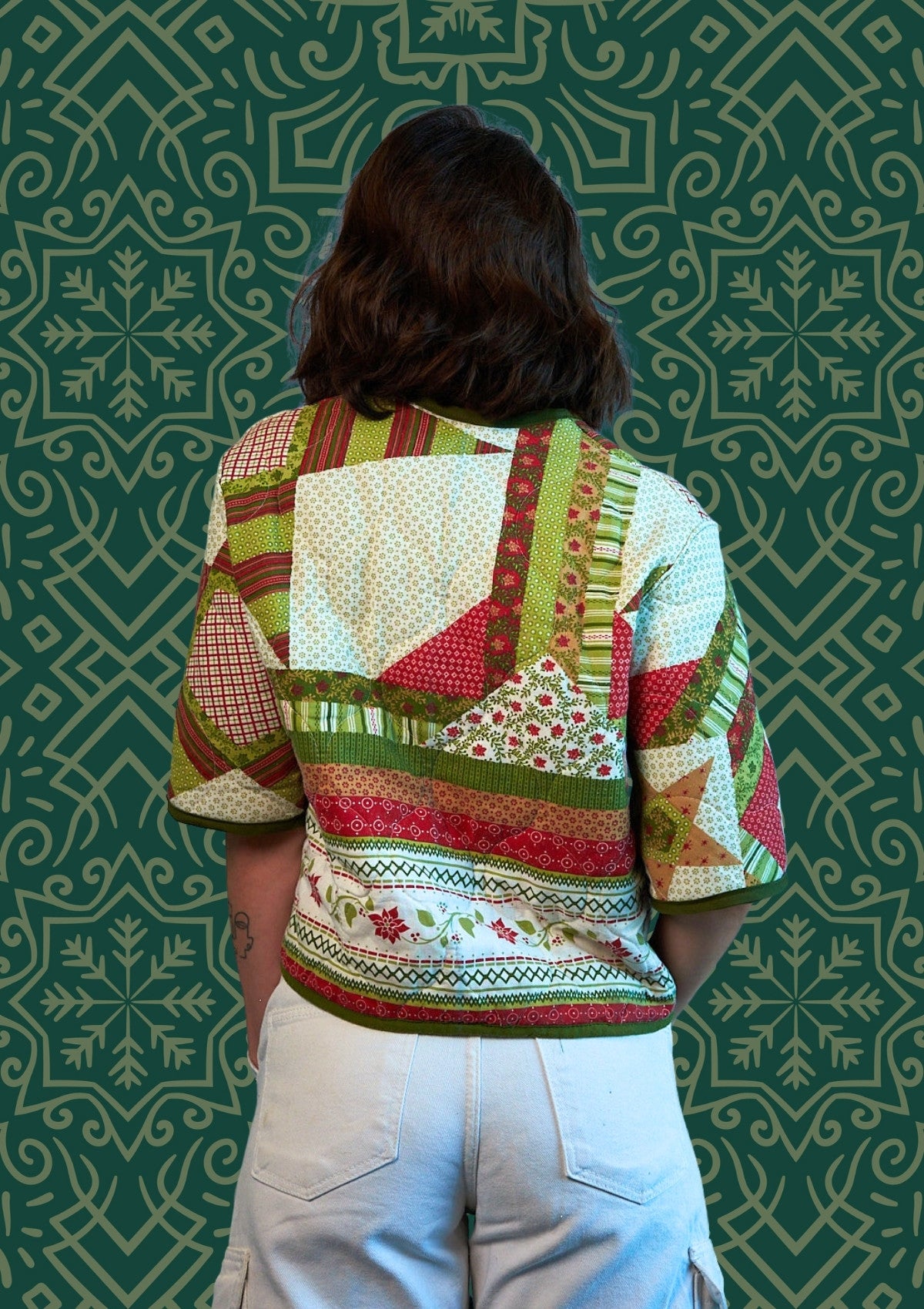 Person wearing a colorful holiday quilted jacket upcycled from comforter against a patterned green background