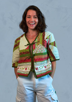 Woman wearing a colorful patterned holiday jacket upcycled from comforter against a light blue textured patterned background