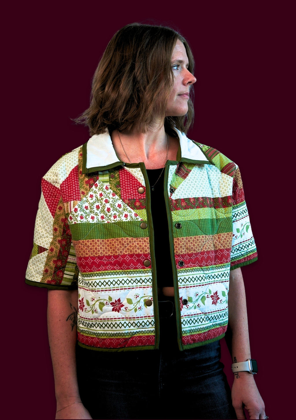 Woman wearing a festive holiday patchwork jacket upcycled from a comforter against a dark background