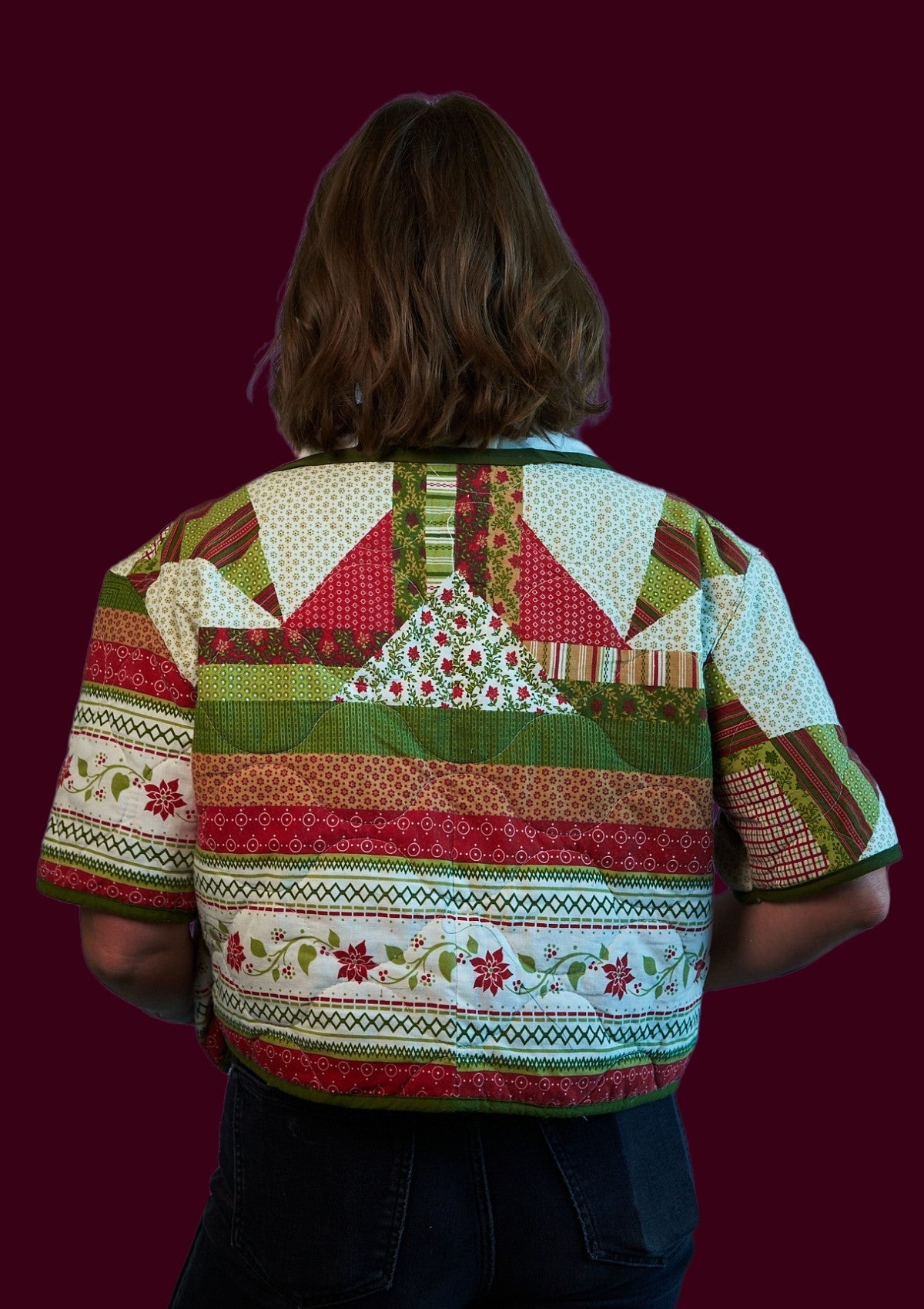 Person wearing a colorful holiday patchwork shirt with a festive patterned design upcycled from a comforter on a dark background