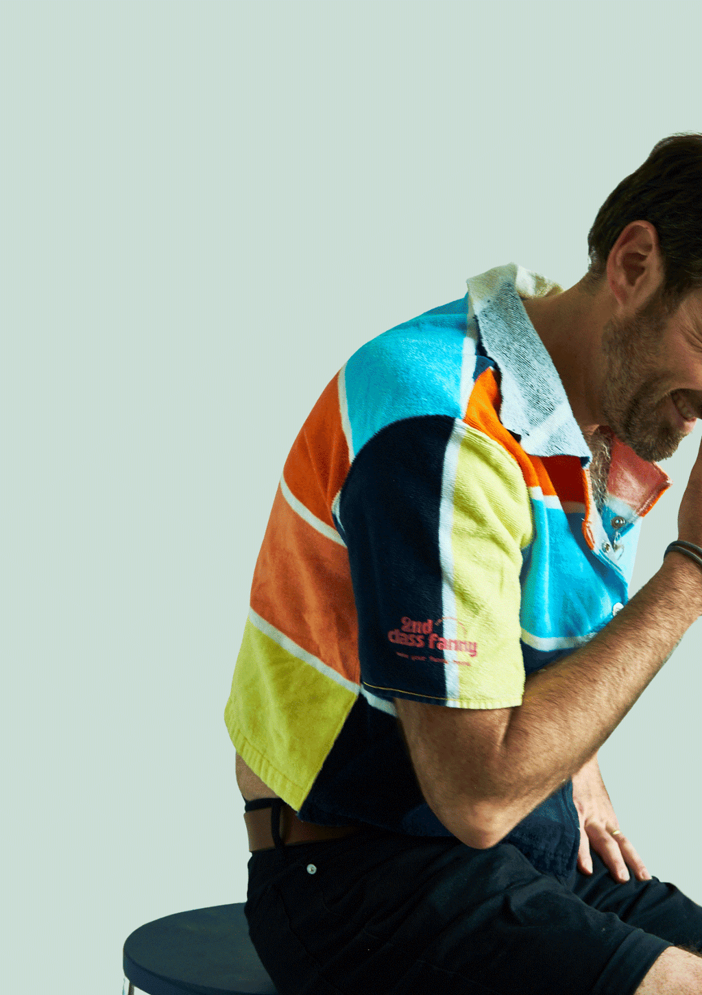 Person wearing a colorful striped shirt upcycled from a beach towel sitting on a chair against a light background