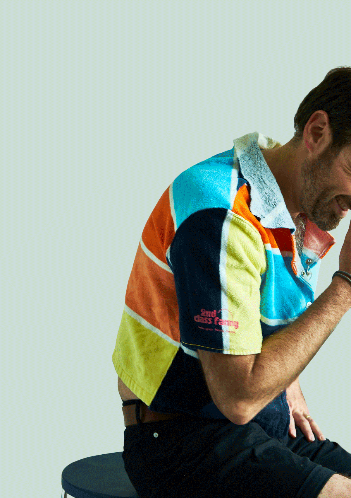 Person wearing a colorful striped shirt upcycled from a beach towel sitting on a chair against a light background
