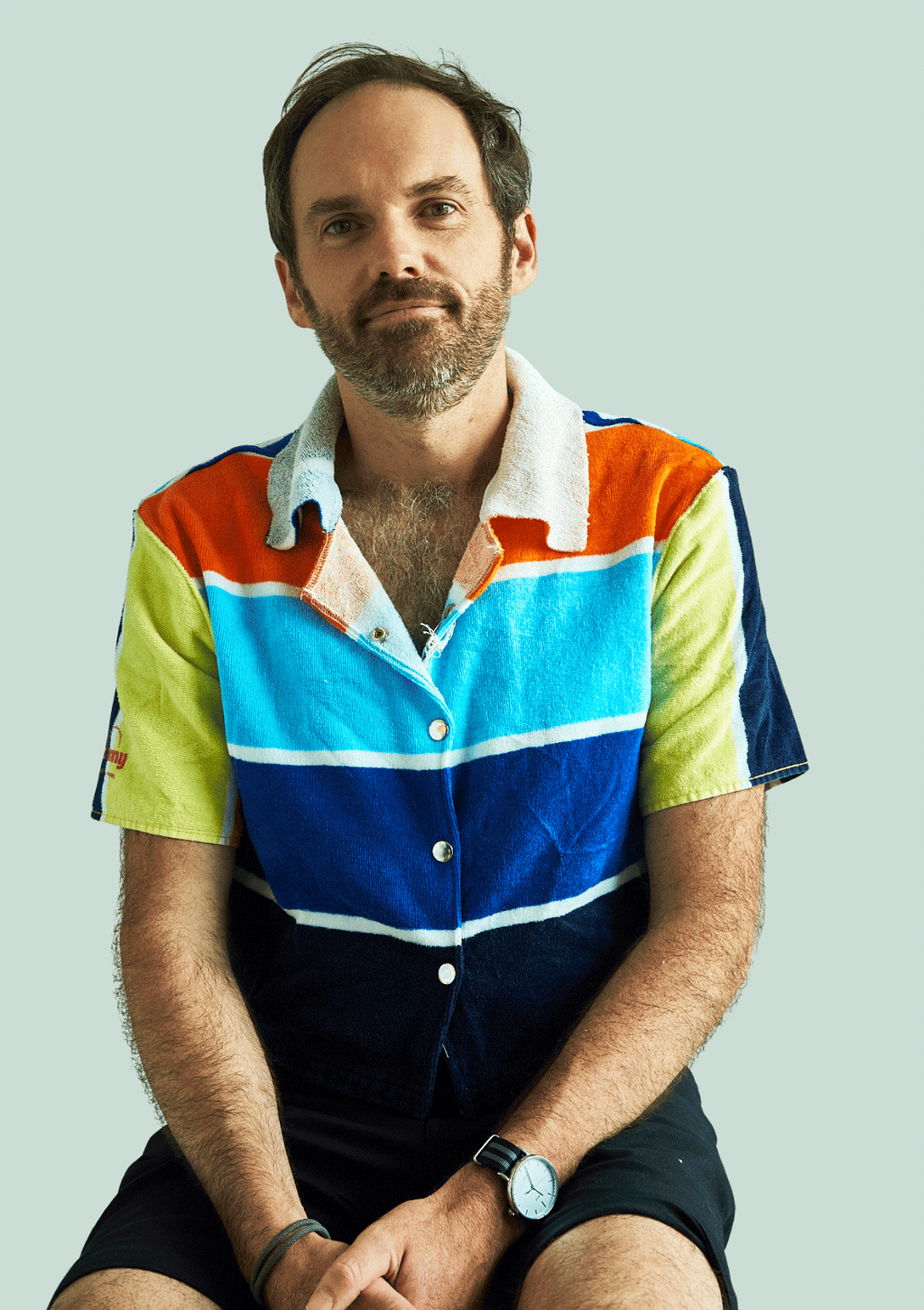 Man wearing a colorful striped shirt upcycled from a beach towel sitting against a light gray background
