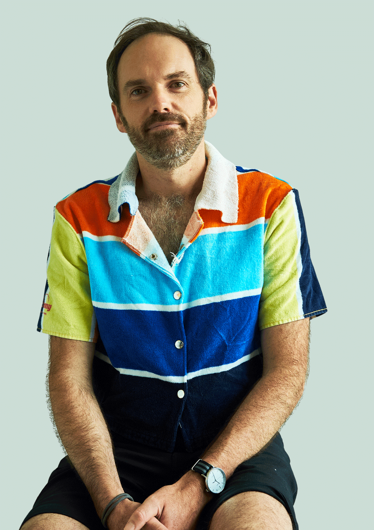 Man wearing a colorful striped shirt upcycled from a beach towel sitting against a light gray background