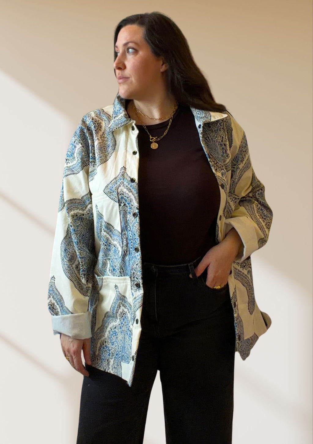 Woman wearing a patterned coat upcycled from a curtain over a dark top and pants against a plain background