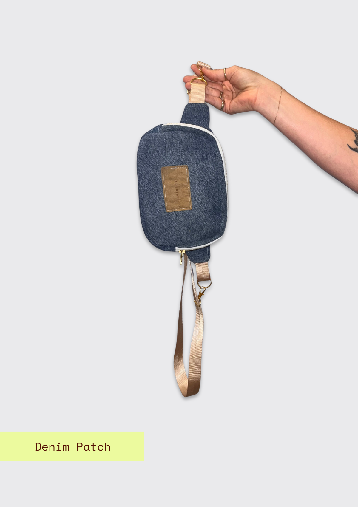 Blue denim crossbody bag with a visible patch on a light gray background