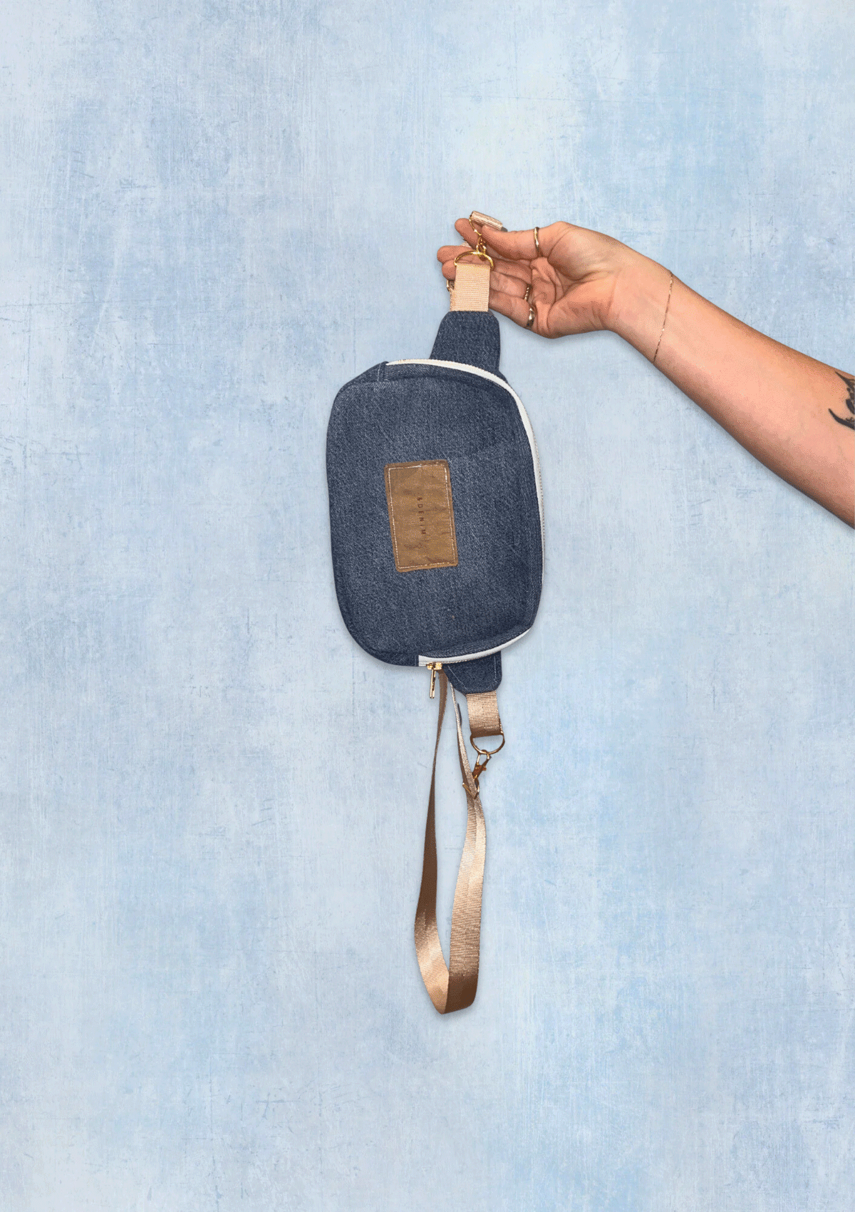 Denim pouch with a strap held by a hand against a light blue background
