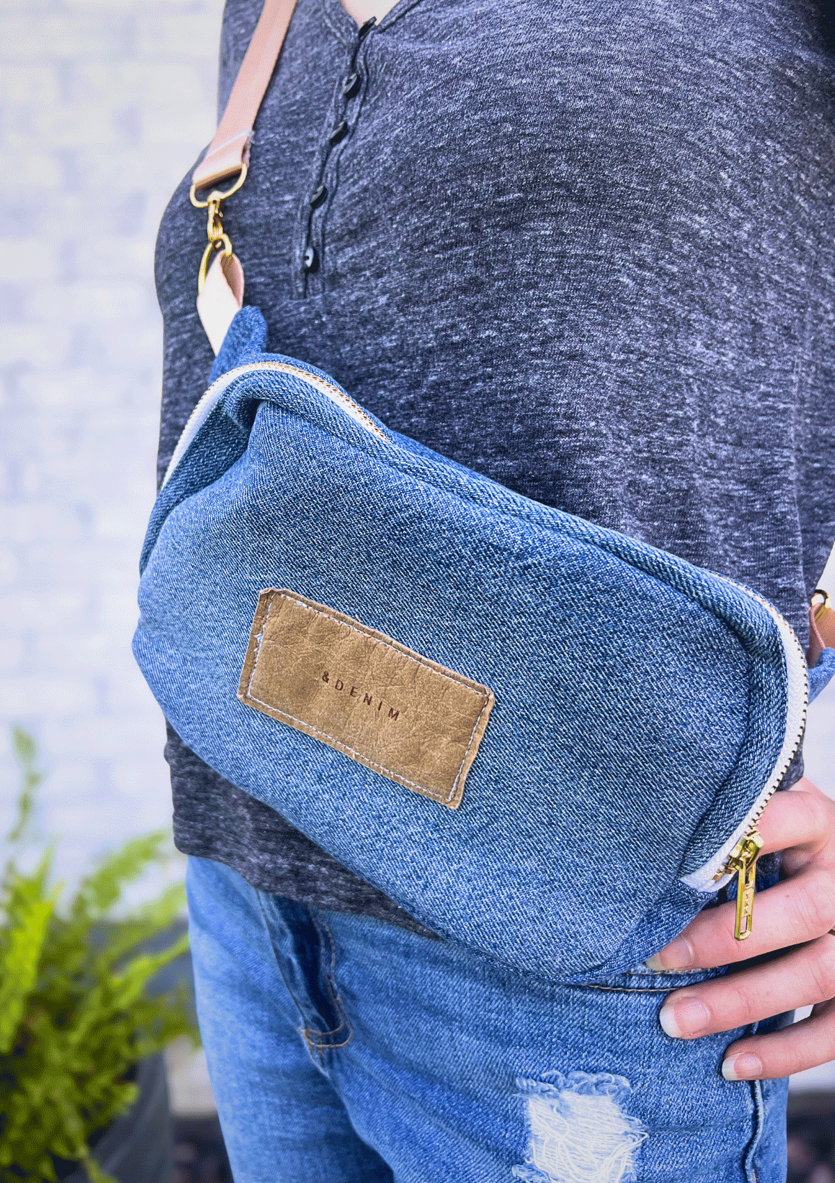 Person wearing a blue denim crossbody bag with a visible brand label.