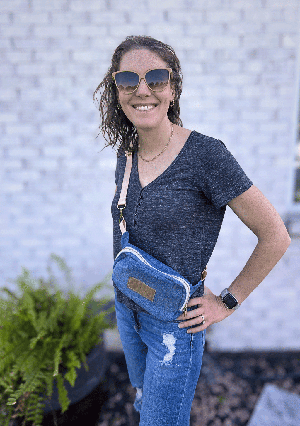 Woman wearing a blue crossbody bag with a textured wall background