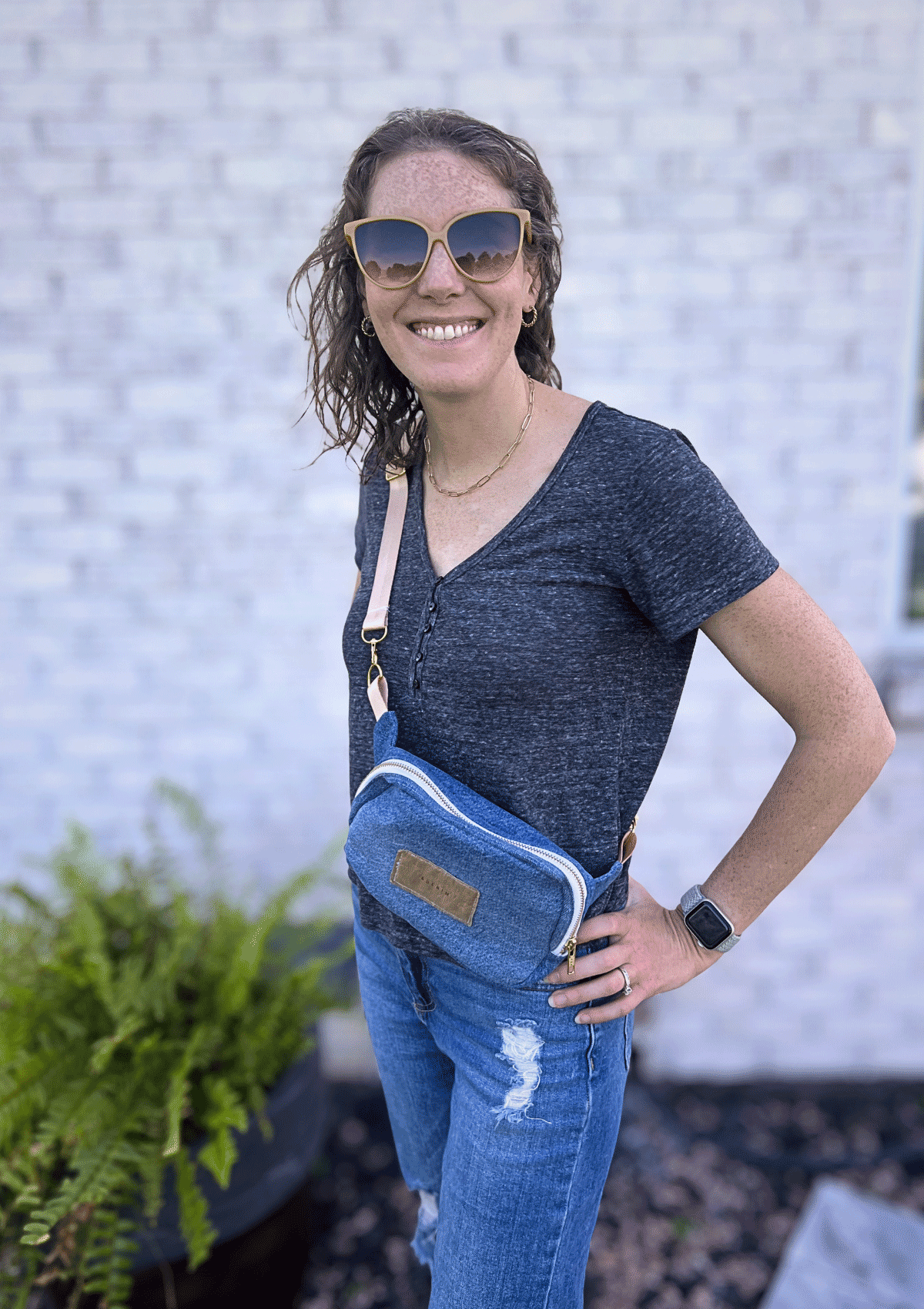 Woman wearing a blue crossbody bag with a textured wall background