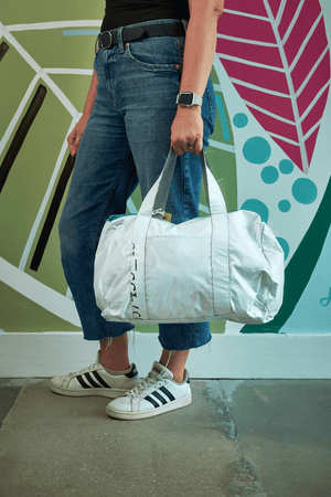 Person holding a white duffel bag with a colorful wall in the background