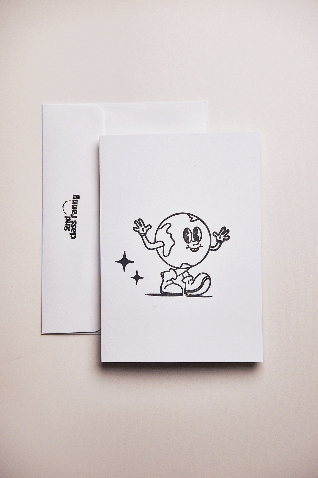 White card with envelope stamped with black illustration of a earth day character on a beige background