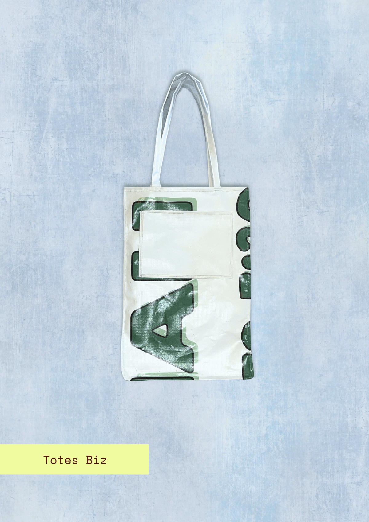 Tote bag with letters pattern, upcycled from an Earth Day Banner on a light blue textured background with Totes Biz branding.
