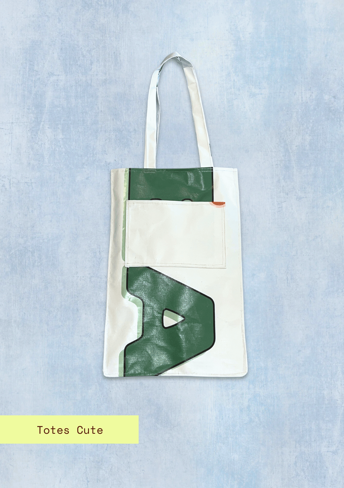 Tote bag with letters pattern, upcycled from an Earth Day Banner on a light blue textured background with Totes Cute branding.