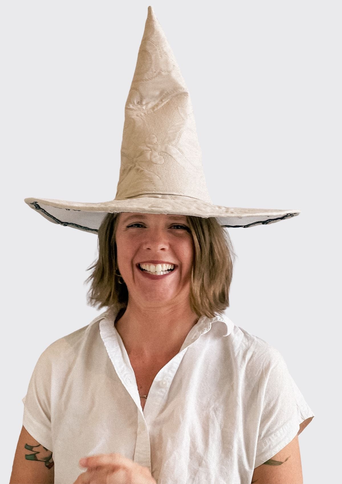 Person wearing a large beige witch hat upcycled from a quilt on a white background
