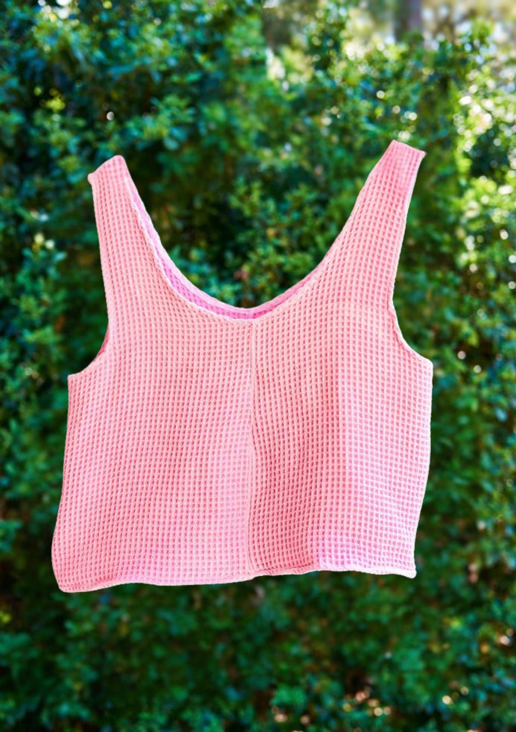 Pink checkered tank top from upycycled towel on a hanger against a green leafy background