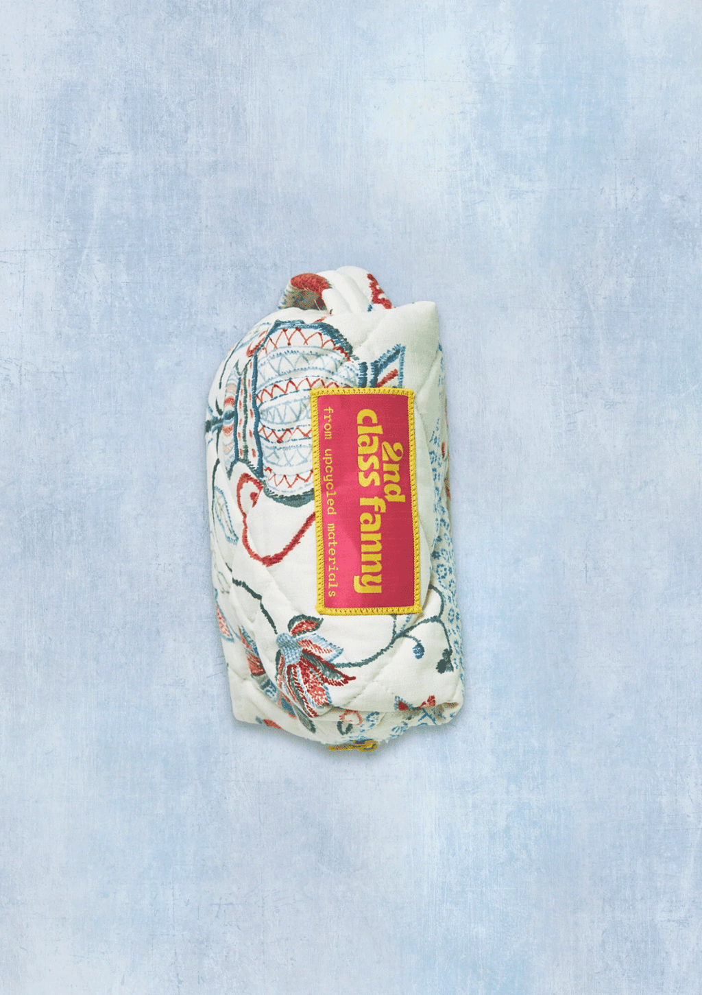 Floral-patterned dobb kit or travel pouch with a visible brand label reads 2nd Class Fanny from upcycled materials on a light blue textured background