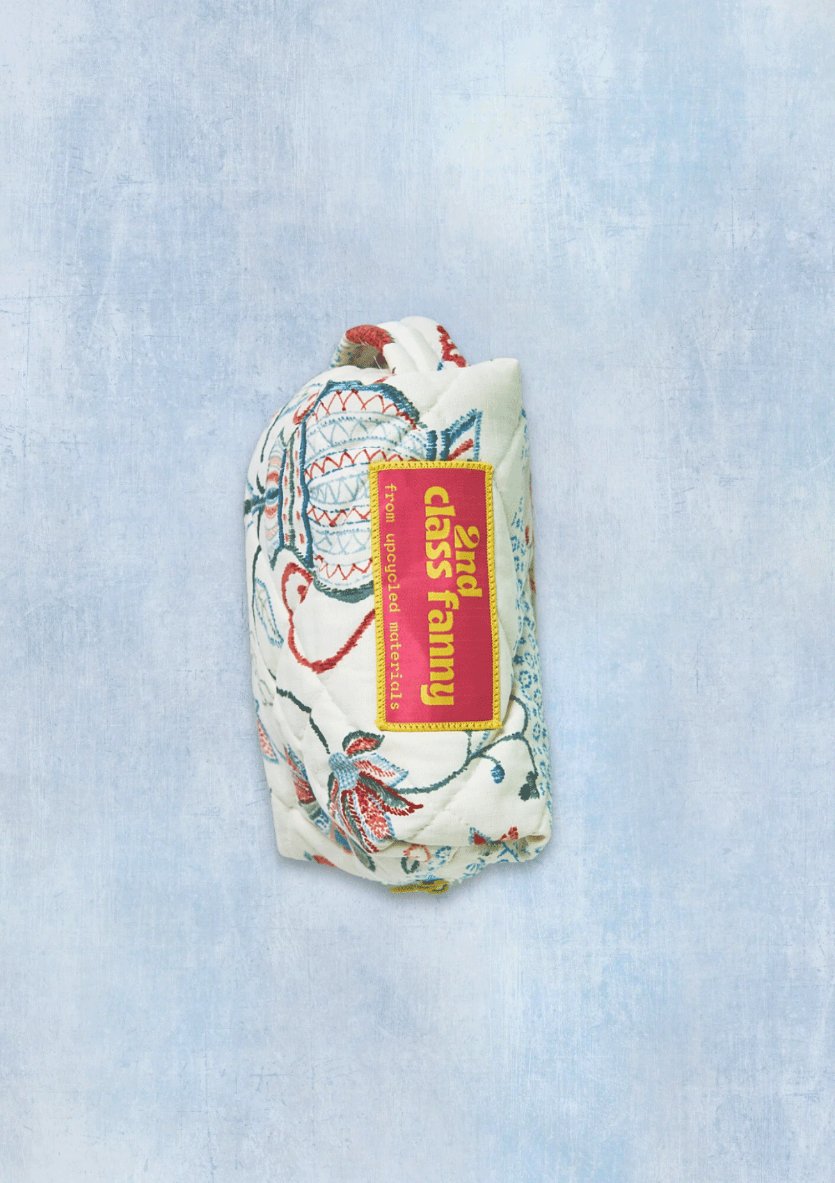 Floral-patterned dobb kit or travel pouch with a visible brand label reads 2nd Class Fanny from upcycled materials on a light blue textured background