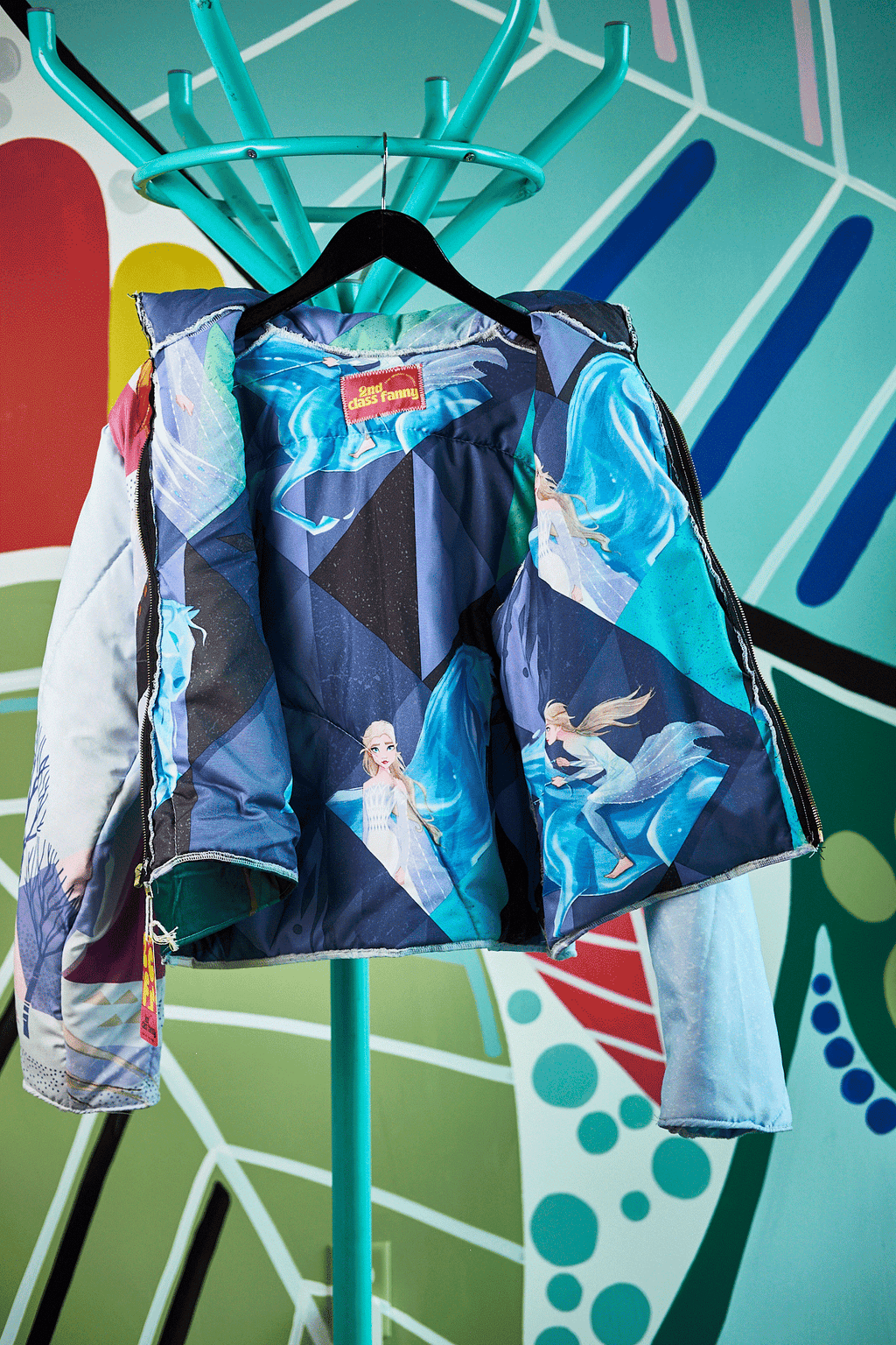 Frozen theme jacket design, upcycled from Frozen sleeping bag  on a hanger against a colorful abstract background