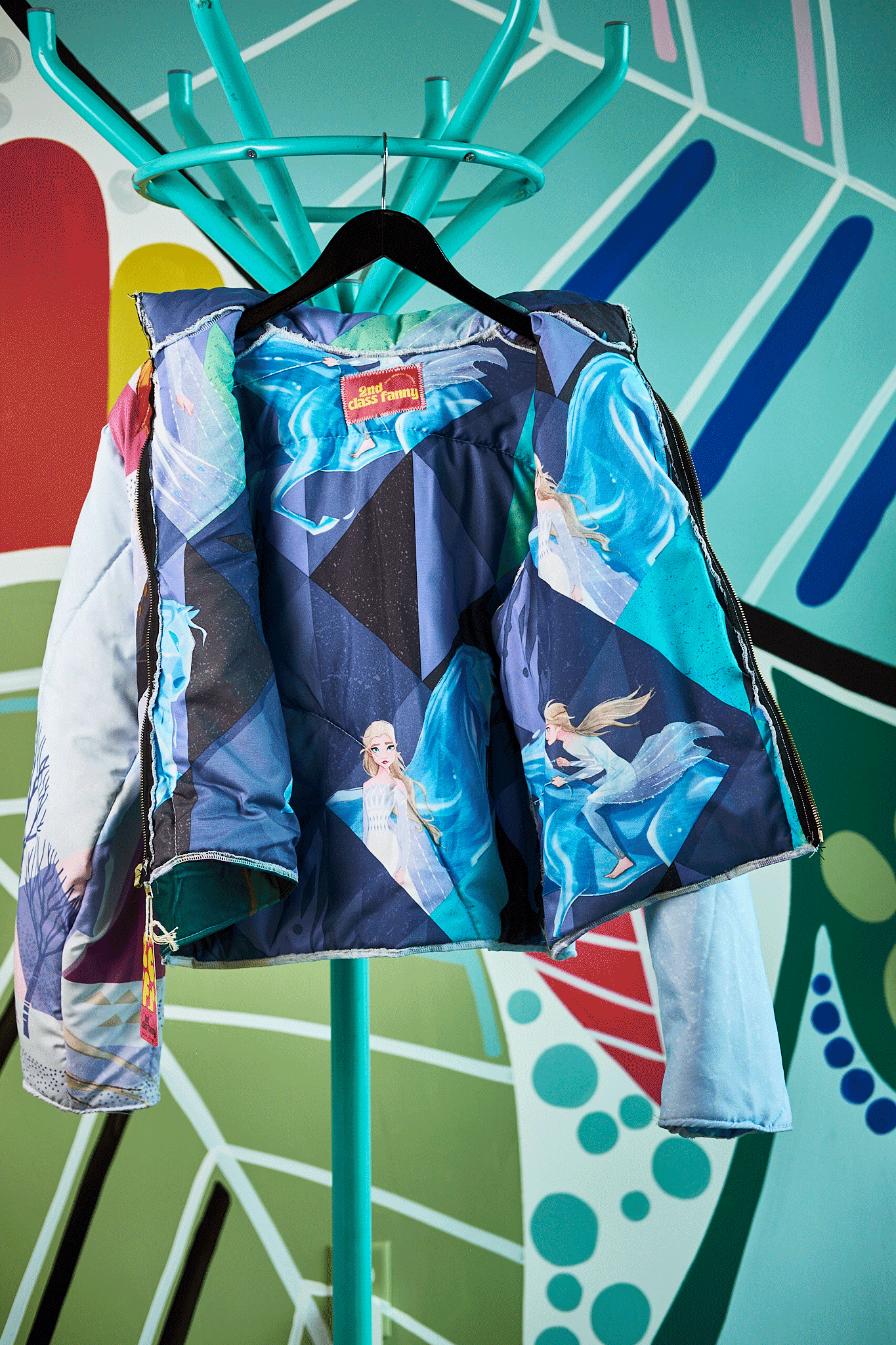 Frozen theme jacket design, upcycled from Frozen sleeping bag  on a hanger against a colorful abstract background