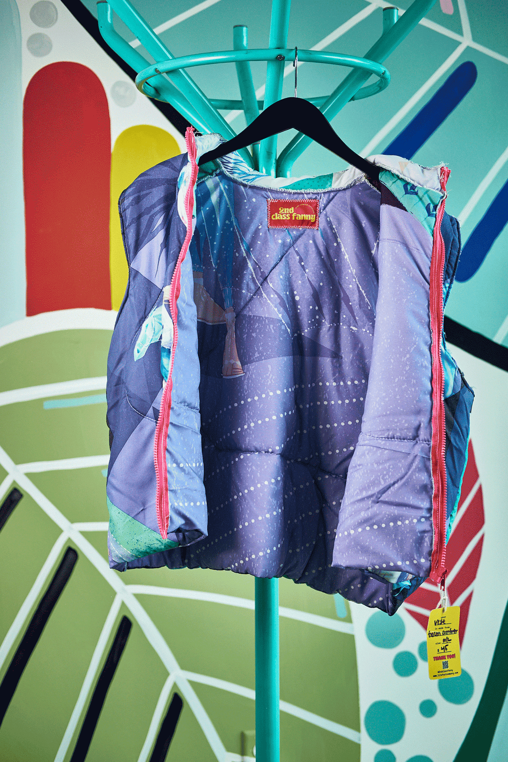 Puffer vest with Frozen theme design on a hanger against a colorful abstract background