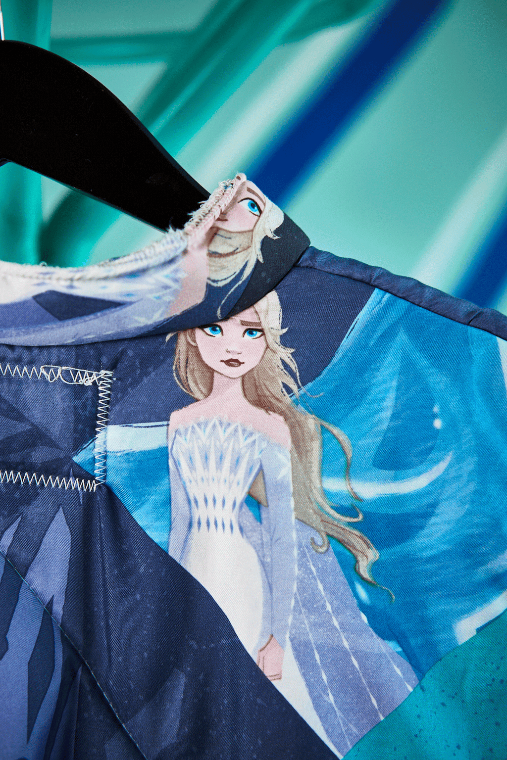 Close-up of a fabric with an illustration of a Frozen character in a blue and white outfit against a teal background upcyled from a sleeping bag