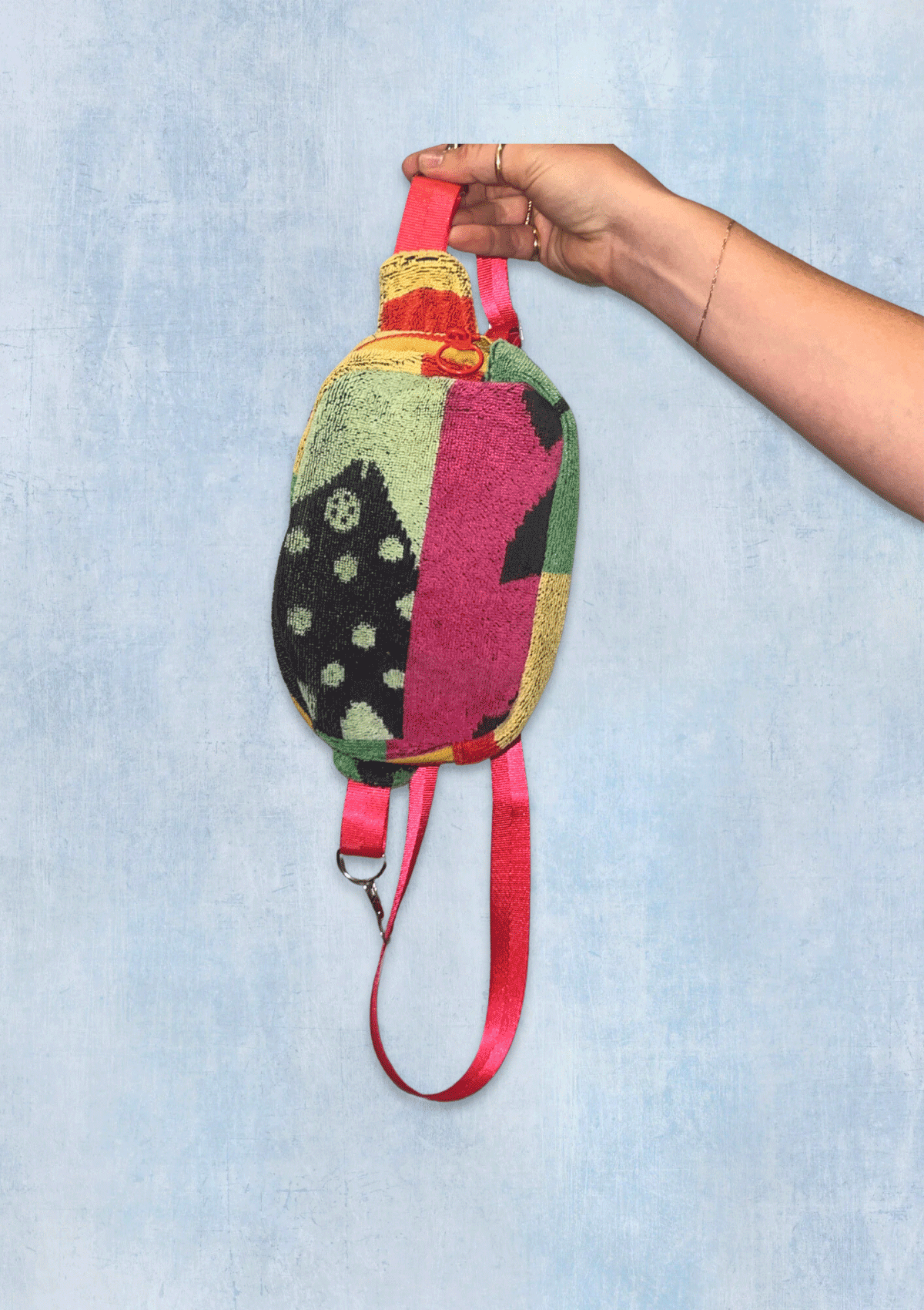 Colorful patterned fanny pack upcycled from beach towel, held by a hand against a light blue denim background