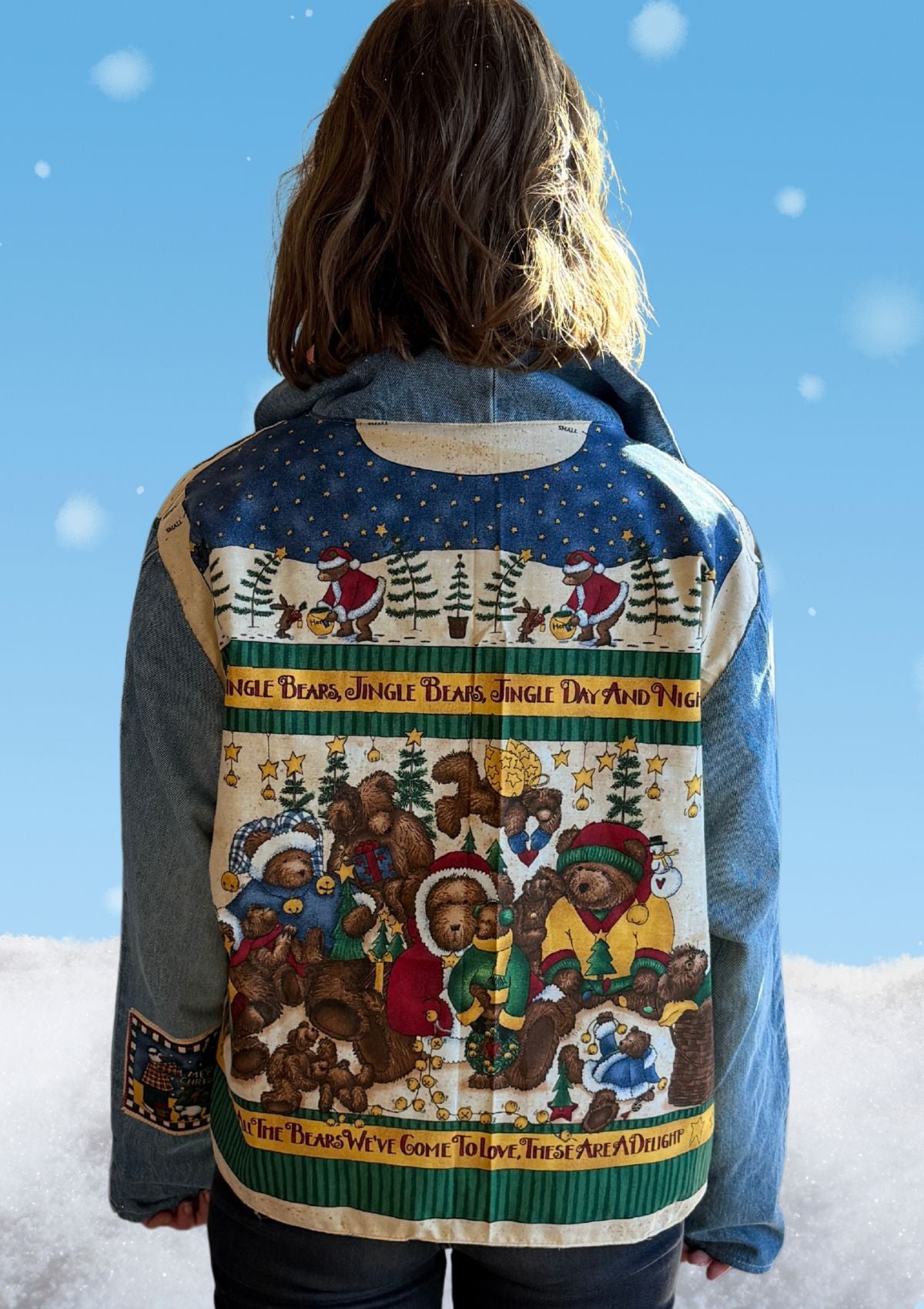 Person wearing a festive denim jacket with teddy bear design upcycled from vintage fabric and denim jeans as sleeves against a snowy background